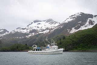 Research vessel Island C in cove with snow covered mountains in the background.