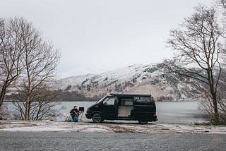 Micro camper by lake with man sat outside in snow