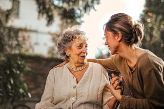 An elderly woman holding the hand of a younger woman.