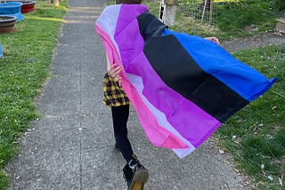 A tween runs with a genderfluid flag flying behind them.