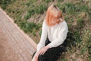 A strawberry-blonde woman sitting outdoors against a hill.