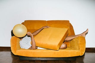 A woman lying on a sofa, trying to hide behind sofa cushions and a ballon