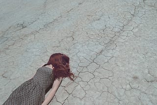 A girl, or possibly doll, laying down on the pavement with her face hidden