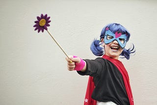 Laughing child with purple hair, red cape, eye mask and wand