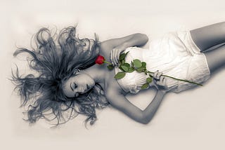 Beautiful young woman lying down with a rose on her chest