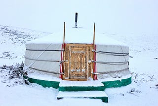 A snowy white yurt with a wooden door.