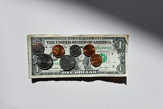 one dollar bill, two quarters, two dimes, three pennies on a white background