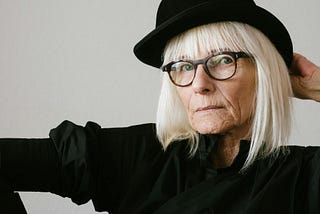 Older woman in black long sleeved top wearing a black hat.