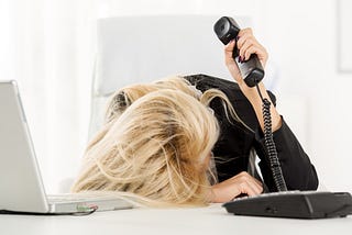 women holding phone with head on desk frustrated with bad work environment.