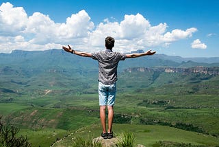 A man opens his arms wide before a vista, representing the world at his fingertips
