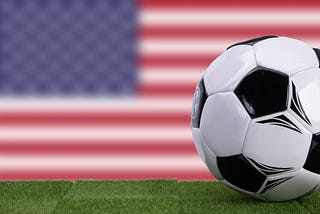 A soccer ball on grass in front of the U.S. flag