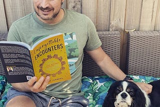 Ash holding his book Unforgettable Encounters, seated next to a dog looking a the camera