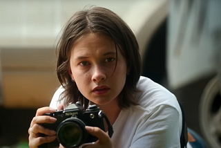 Jennie (played by Cailee Spaeny) holds a Nikon camera with a concerned look on her face.
