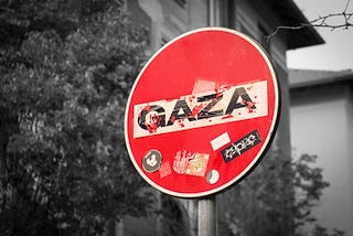 A red stop sign with the word Gaza across the white bar in middle against a black and white background of houses and trees