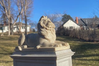 Miniature statue of a lion lying on a pedestal with his head facing the sun.