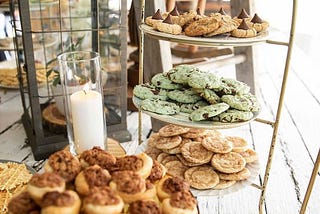A variety of cookies on a multitiered serving rack next to a candle on a buffet table.