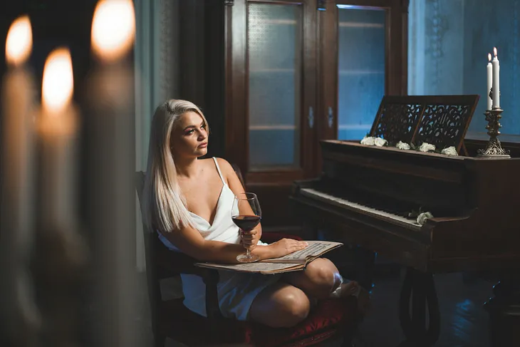 Woman wearing lingerie and holding wineglass sits near piano by candlelight