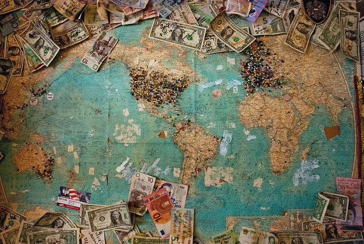 A map of the world with currency from all around the world laying on it.
