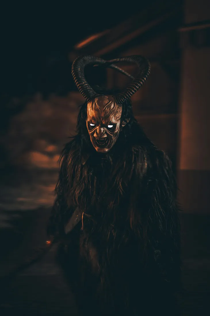 A demon covered in gorilla-like fur, with white-glowing eyes, and long curving horns. Pointed teeth are revealed in a snarling mouth.