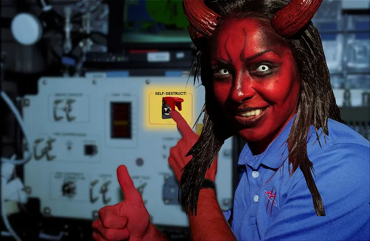 A photo taken on the Space Shuttle, showing an astronaut pointing at a switch on a control panel. The photo has been altered. The astronaut’s head has been replaced with a grinning, horned devil-woman’s head. The switch has been replaced with a red-guarded toggle switch, labeled ‘SELF-DESTRUCT!’ The astronaut’s arms have been colorized to match the brick-red skin of the demon head. The background has been slightly blurred. Image: Mike (modified) https://www.flickr.com/photos/stillwellmike/1567
