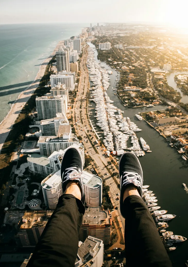 Aerial view of the coastline of Miami, taken from someone who has their legs hanging outside what is probably a helicopter.