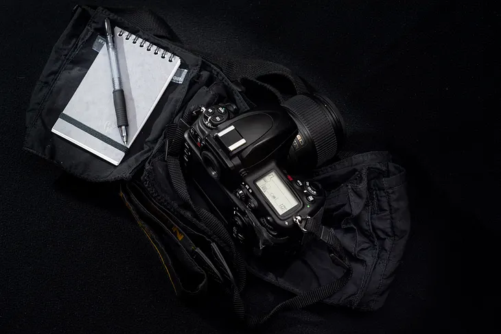 A display of a DSLR camera and a paper notebook sitting on a camera bag.