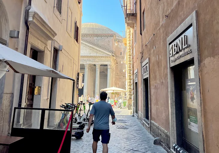 A man with a sweaty shirt walks towards the Pantheon in Rome, Italy on one of the many one-hundred degree days in June 2022