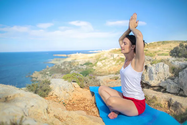 A woman meditates high on a clifftop