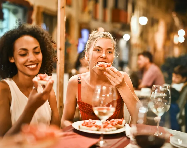A Black woman and a white woman eat next to each other in a restaurant.