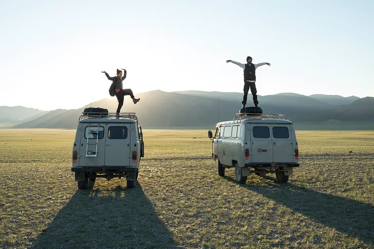 Two vintage camper vans in desert with people dancing on the roofs