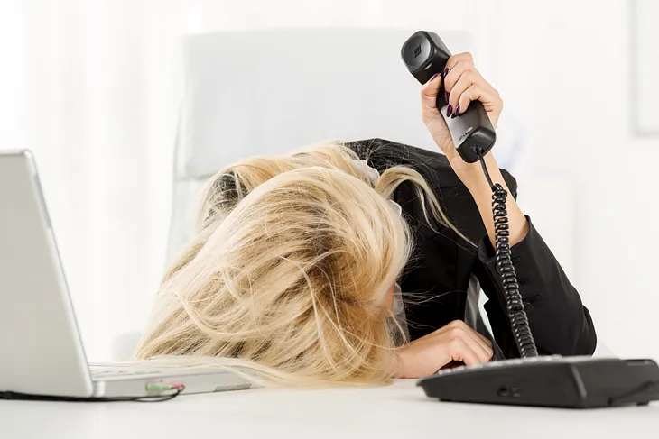 women holding phone with head on desk frustrated with bad work environment.