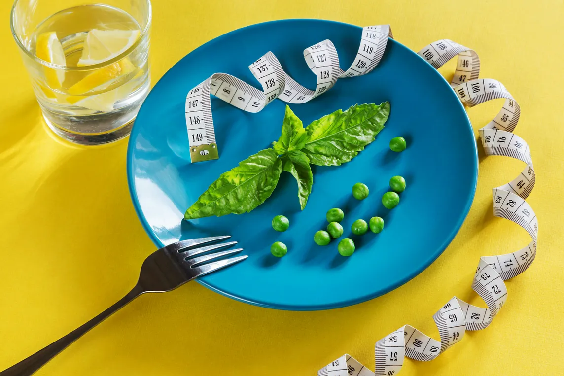 A plate and fork with just a couple of green leaves, a few peas and a curled tapemeasure.
