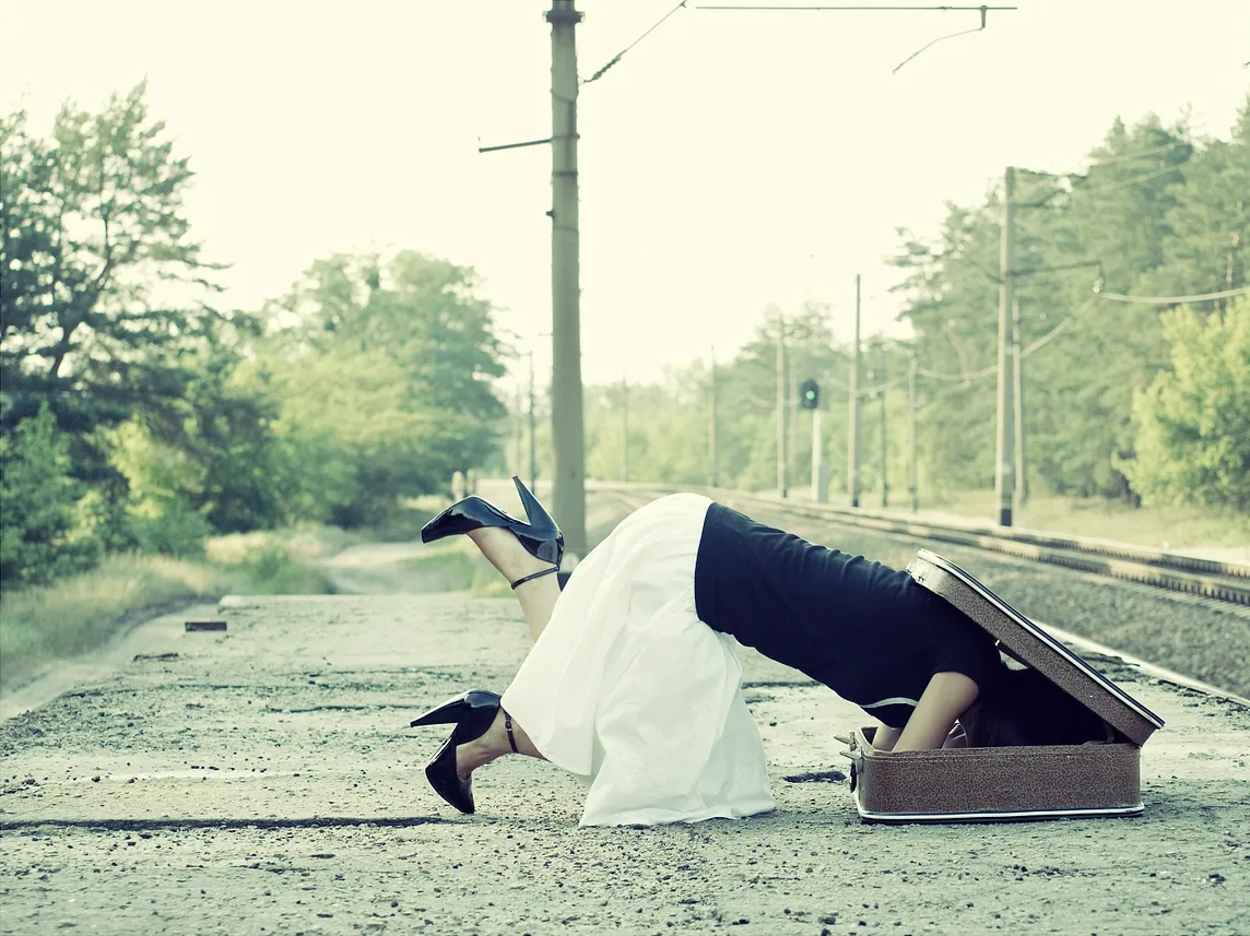 A woman with head in suitcase in front of reailroad track to symbolize hiding her accomplishments