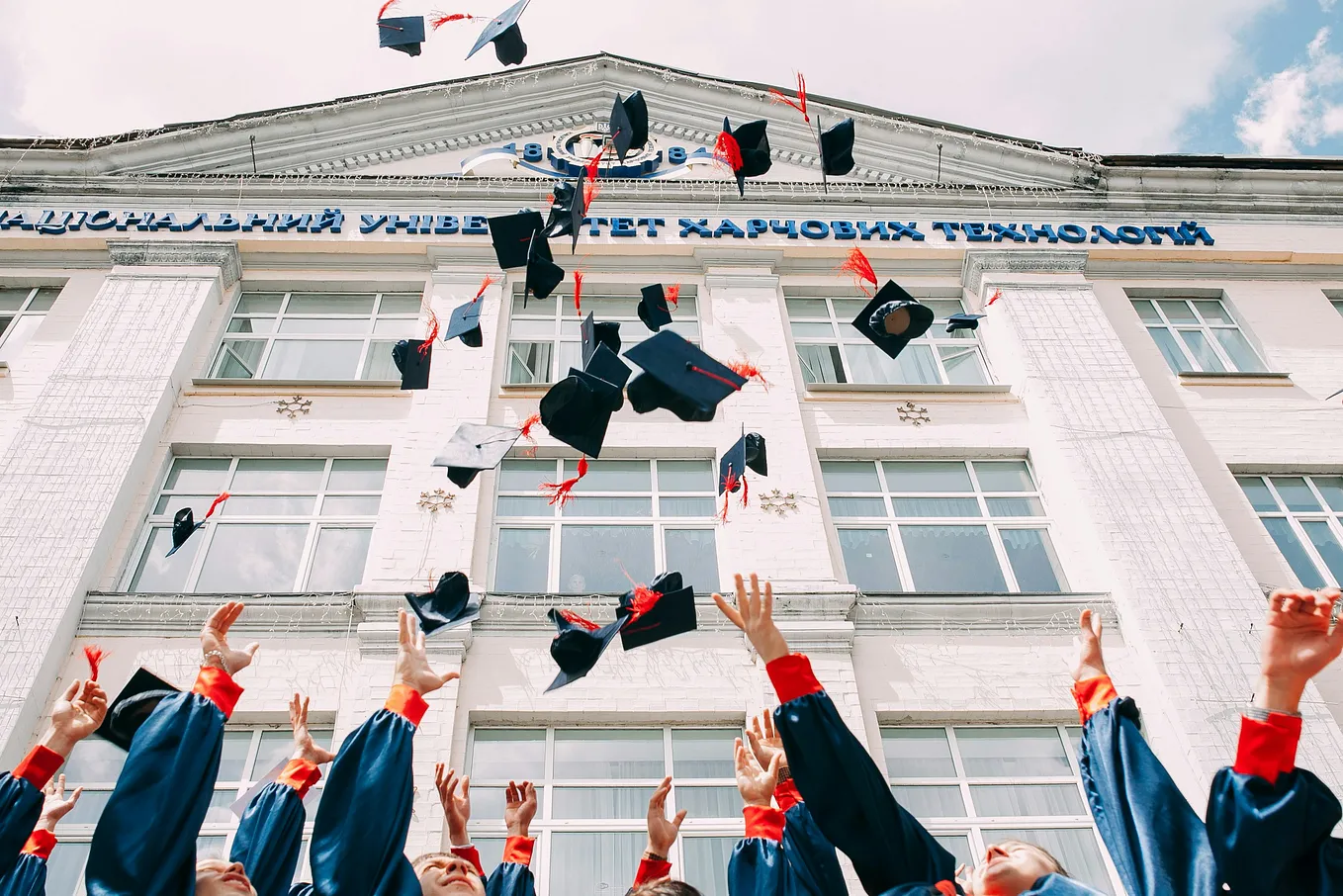 Several graduates throwing their mortarboards in the air in front of a white building