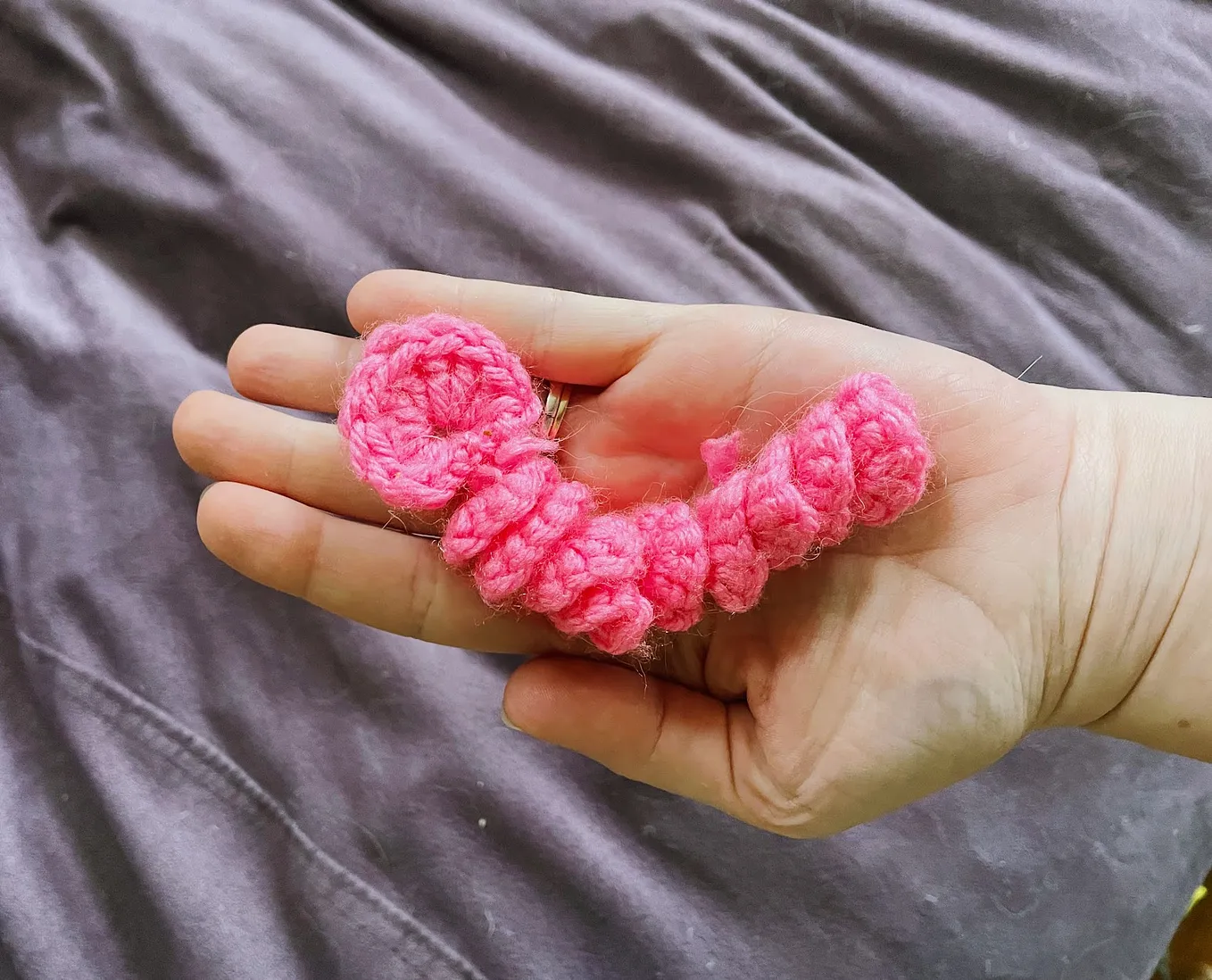 A pink crochet “worry worm” held in an open palm