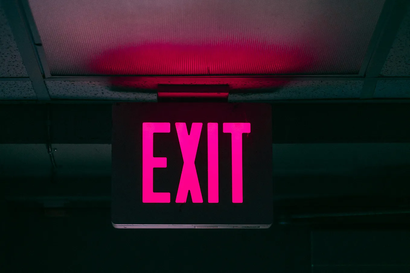 Neon pink “EXIT” sign illuminated against a dark ceiling
