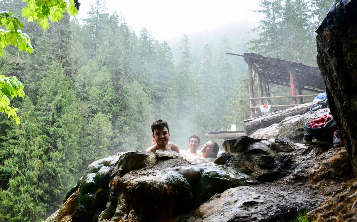 Three people lying in a hot spring surrounded by Oregon forest.