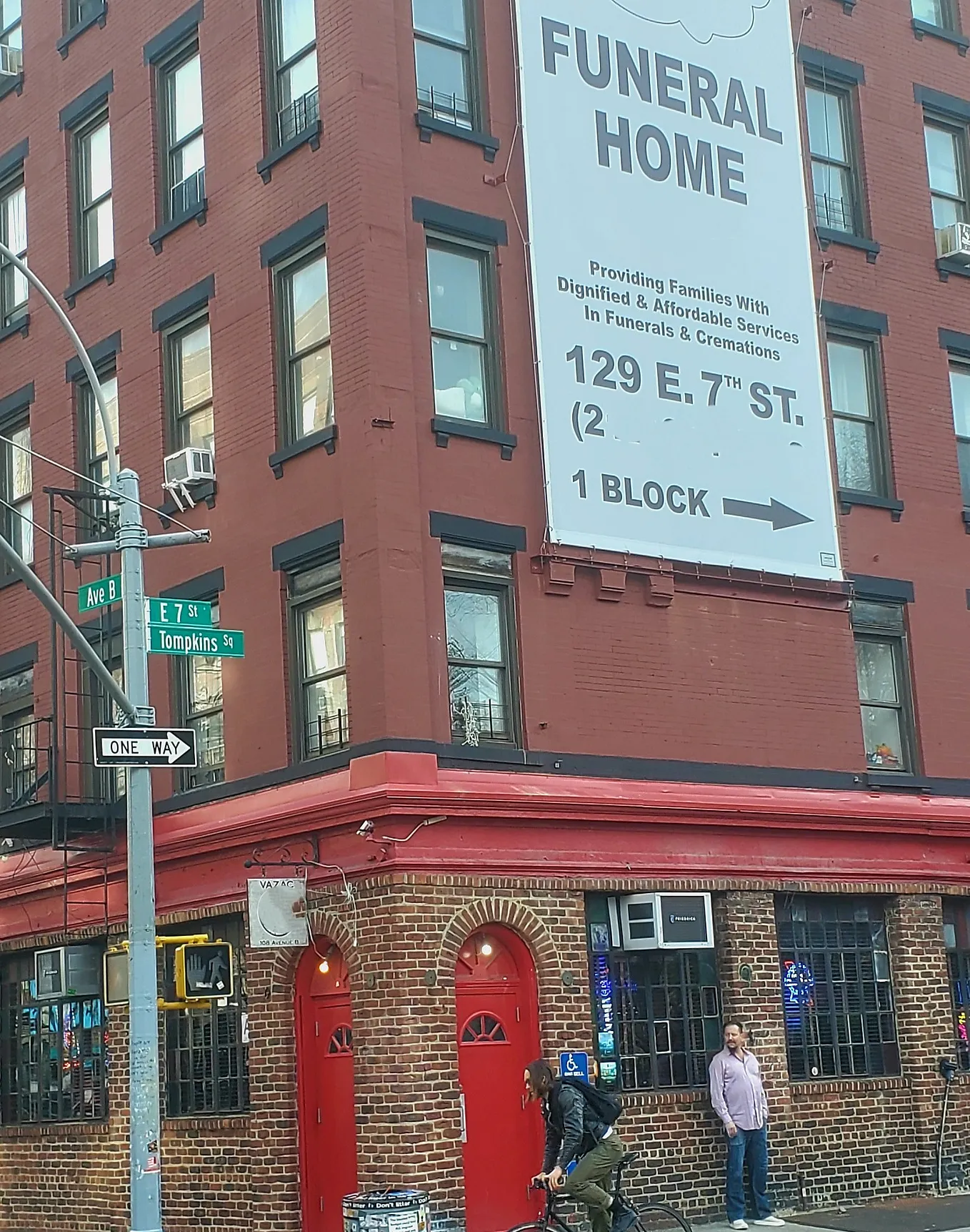 A corner bar in NYC is situated underneath an ad for a funeral home, one block away